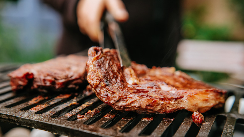 A person flips juicy and saucy steaks on a grill