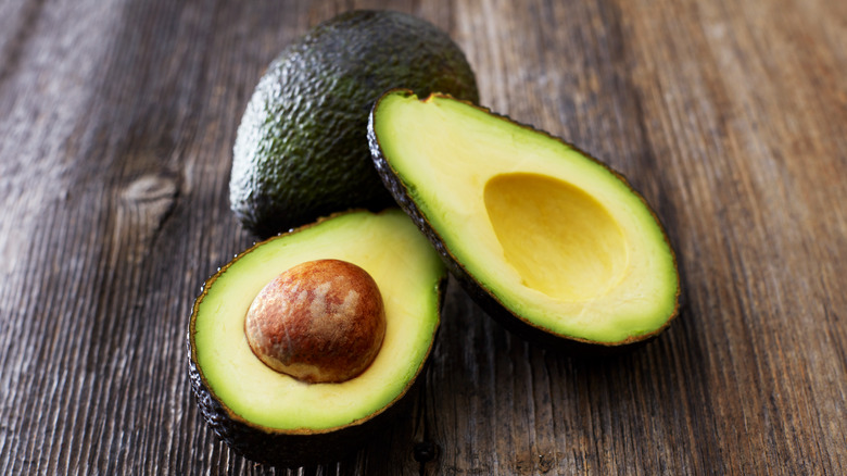 two avocados on a table with one sliced open