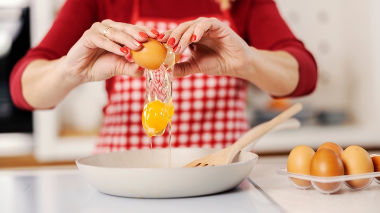 woman cracking egg into pan