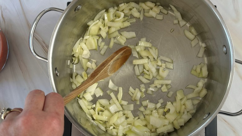 hand stirring onions in pot