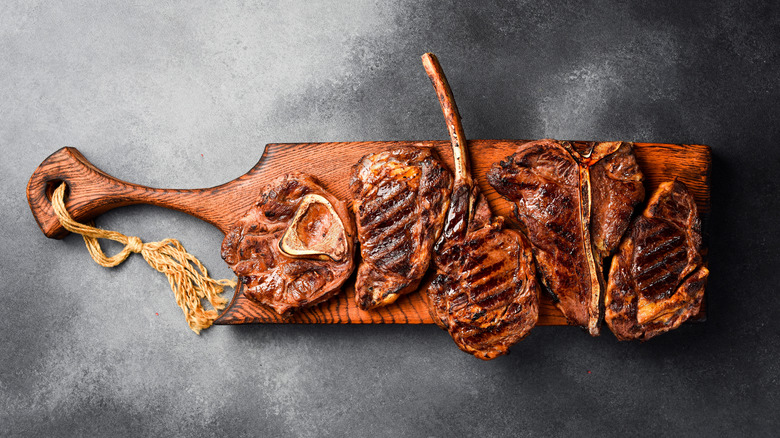 A variety of different cuts of grilled steak on a wooden board