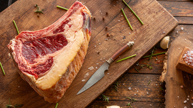 Dry-aged steak on a wooden cutting board next to a knife