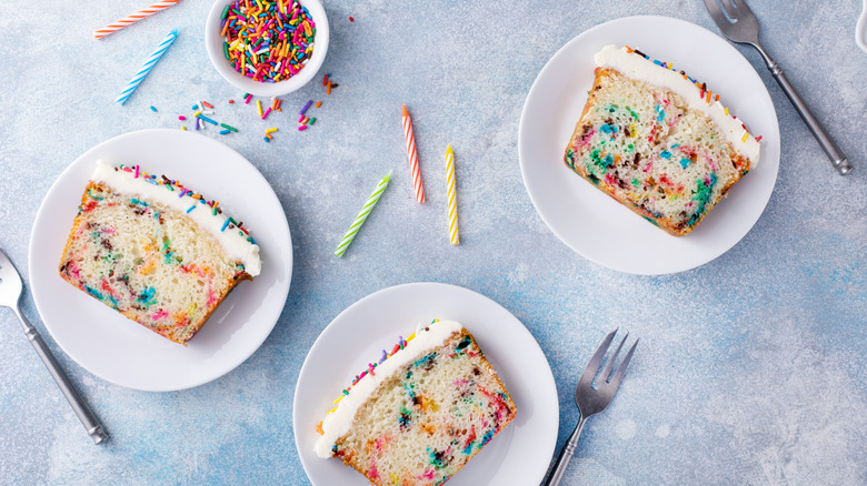 Slices of white birthday cake with rainbow sprinkles and candles