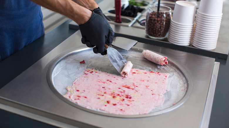 someone with gloved hands scraping ice cream into rolls from an ice pan.