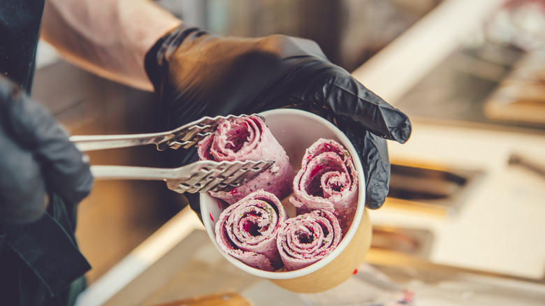 A person places rolled ice cream into a cup