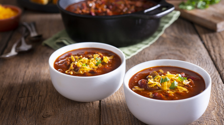 chili in bowls with cheese on top, pot of chili in background