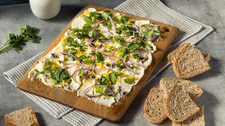 A butter board with onions, herbs, and bread