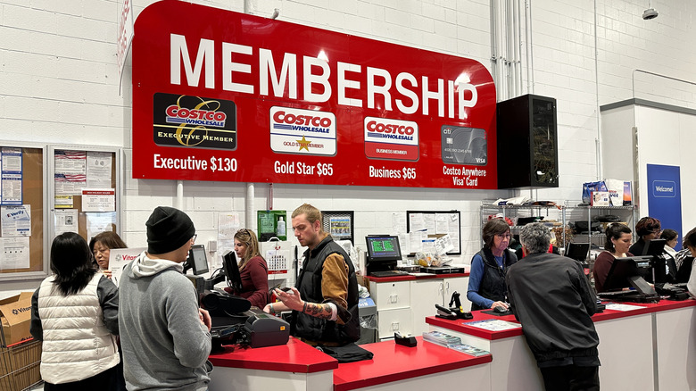 Costco members stand at a membership counter while employees assist them