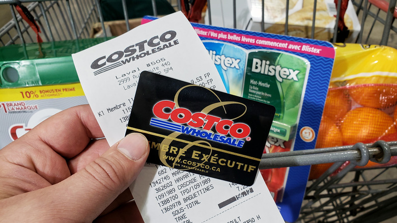 Hand holding a black and gold Costco executive membership card and a receipt