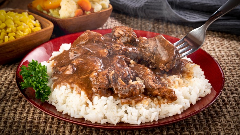 a plate of beef tips and gravy on a bed of white rice