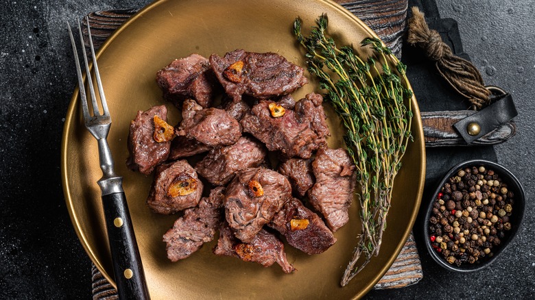 Seared steak tips on gold plate next to rosemary bunches