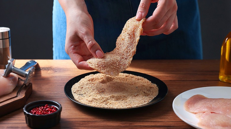 Hands dredging meat cutlet in bread crumbs