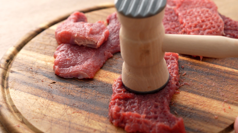 A few pieces of tenderized steak with even small cuts across their surface on a light wooden surface