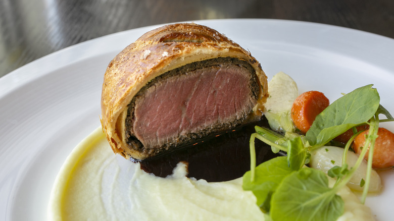 Slice of cooked beef Wellington on plate with vegetables