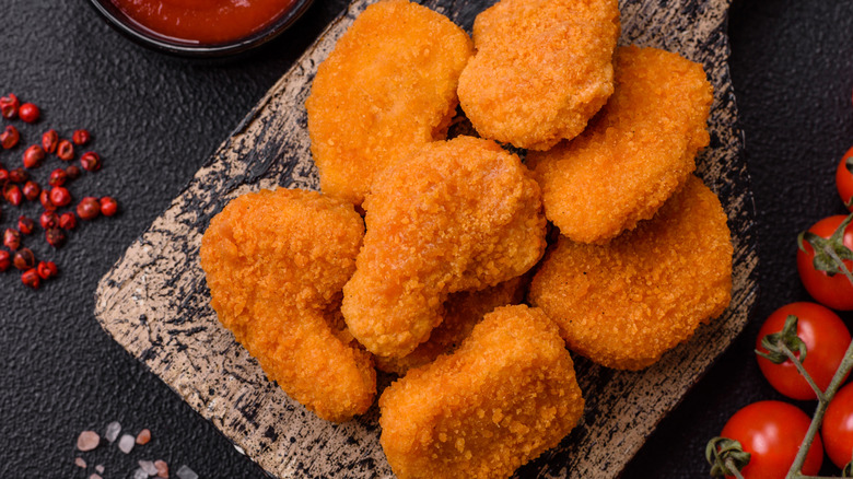 Chicken nuggets on a wooden panel with cherry tomatoes and ketchup beside it