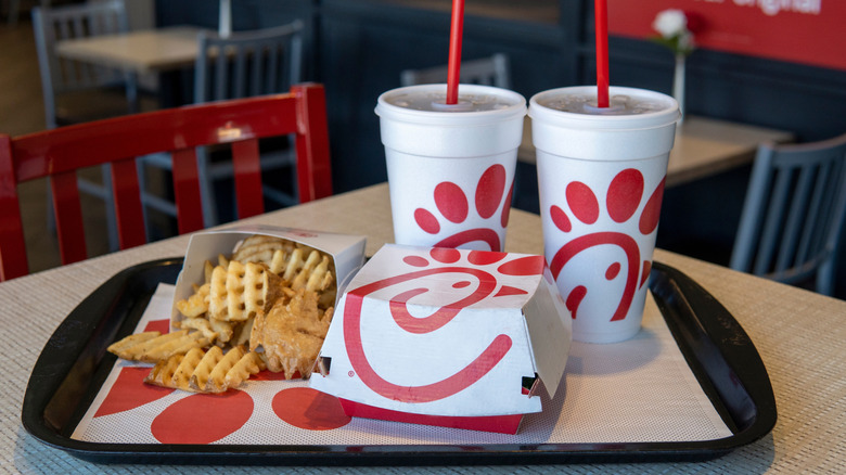 A tray contains Chick-fil-A Waffle Potato Fries, a closed sandwich container, and two fountain drinks