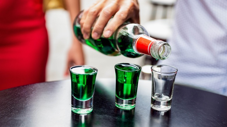 Bartender pouring shots of green liqueur 