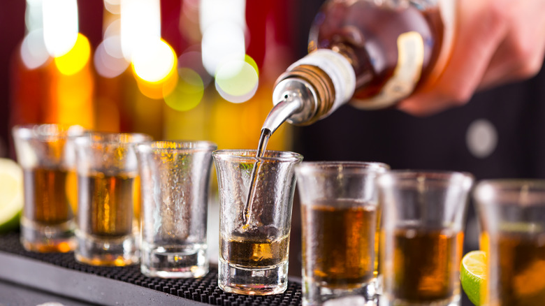 Bottle of liquor being poured into shot glasses