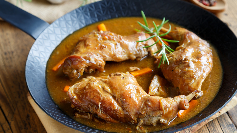 A roasted rabbit sits in a bed of stewed gravy and vegetables