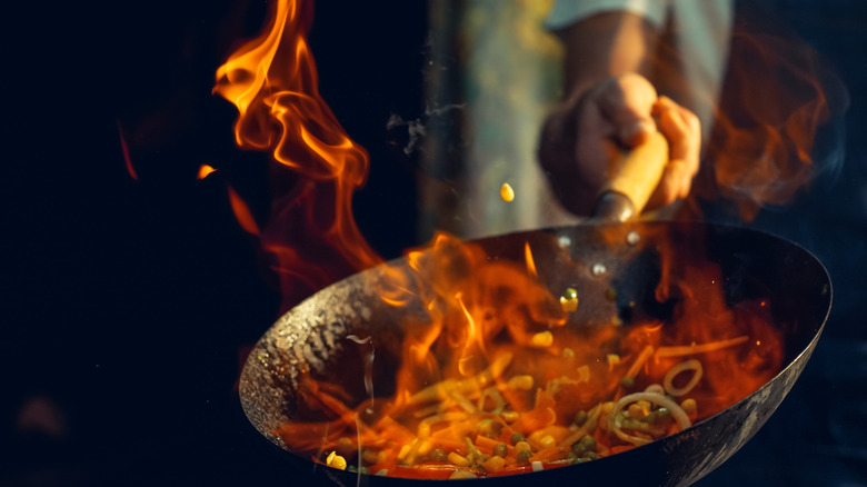 A chef cooks a flaming wok of stir fry.