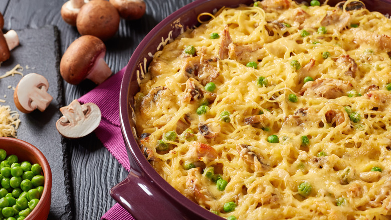 Chicken tetrazzini in a casserole dish next to mushrooms and a bowl of peas