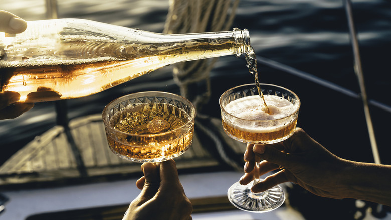 person pouring champagne into cocktail glasses on a boat