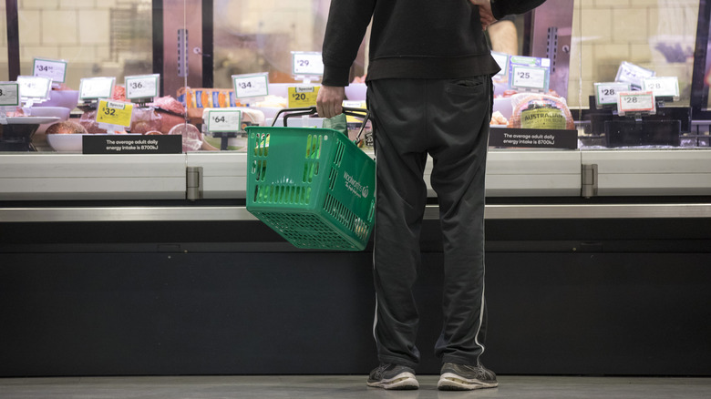 man at meat counter at grocery store, holding a grocery basket