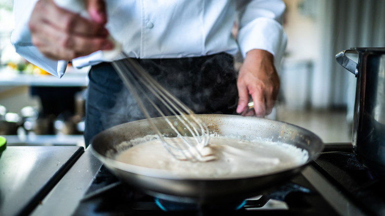 chef whisking sauce in pan over low heat