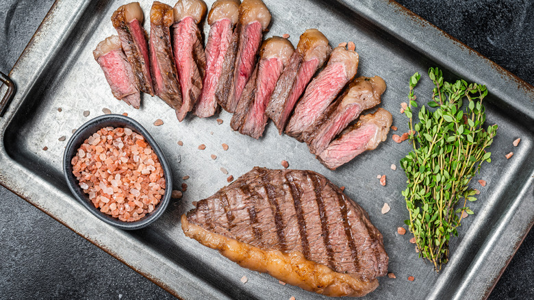 Grilled and sliced picanha steak on a steel tray with salt and herbs