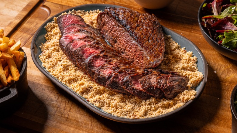 Grilled and sliced picanha steak on a steel tray with salt and herbs