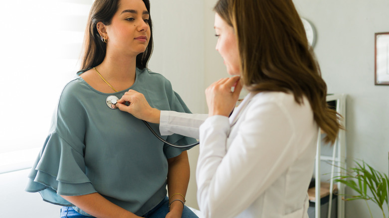 Female doctor listens to female patient's heart with stethoscope