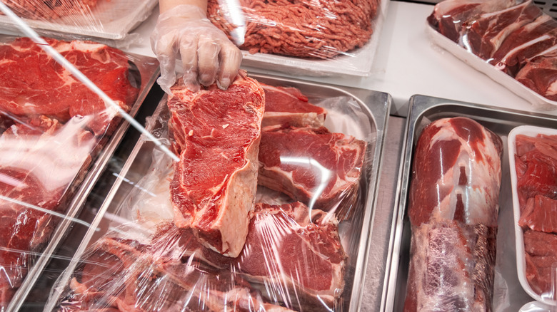 Butcher presents a cut of steak in meat display case