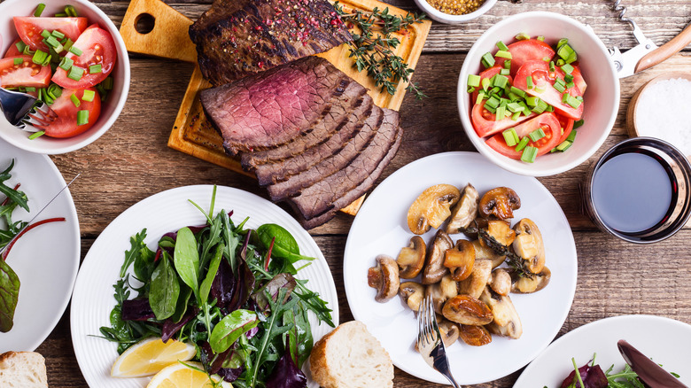 Sliced steak, lettuce salad, and vegetable dishes on a wooden table