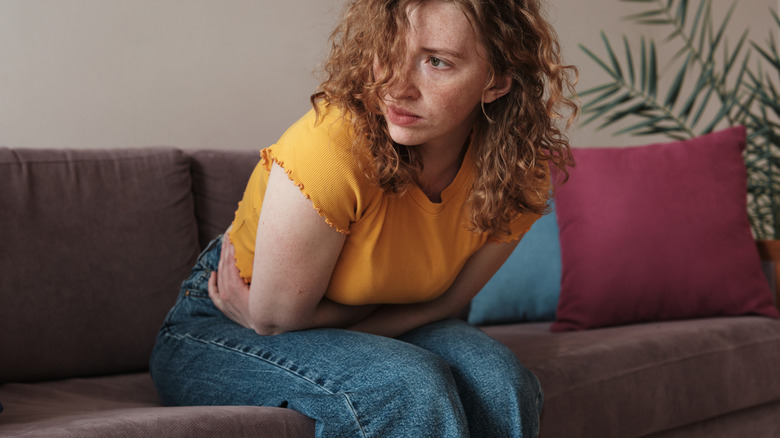 Woman in yellow T-shirt holds her stomach in pain