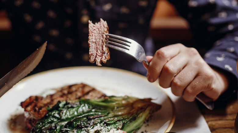 Person holding a fork with a bite of steak over his plate