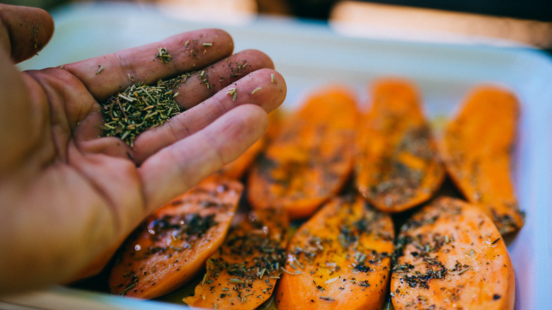 hand holding Italian seasoning over sweet potatoes