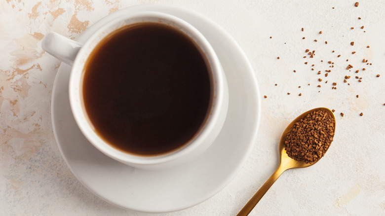 A cup of coffee next to a spoon of instant coffee powder