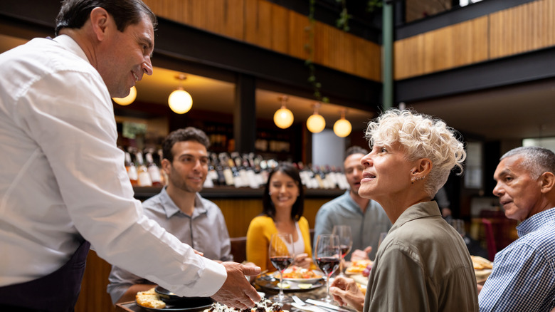 busser speaks to customers at restaurant table