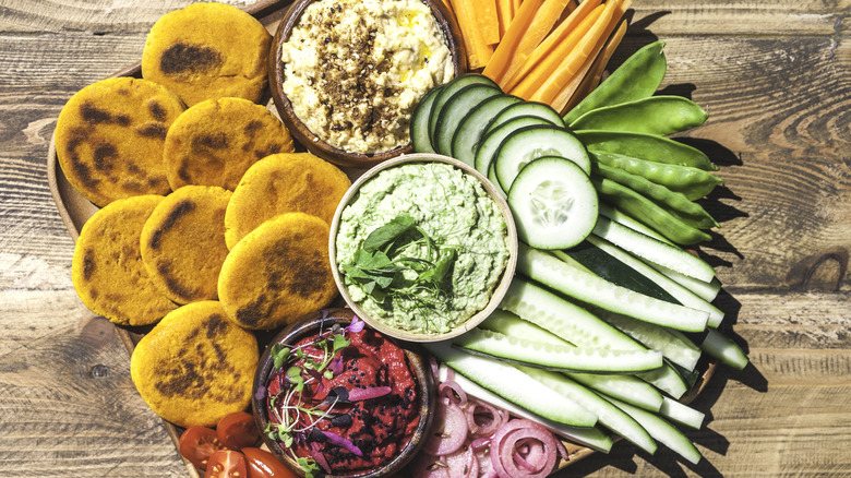 A veggie platter including carrots, cucumbers, snap peas, tomatoes, and dips