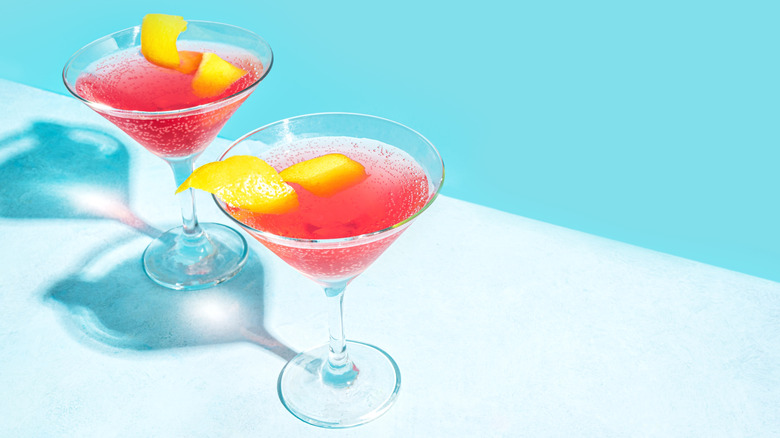 Two pink cosmopolitan cocktails in martini glasses, garnished with lemon peels