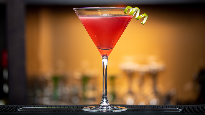 Red cocktail in martini glass with lime curl garnish