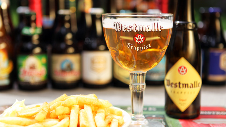 A bottle and glass of Brouwerij Westmalle's Trappist Tripel next to a plate of fries on a table.