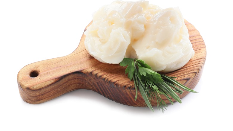beef tallow and herb sprigs on wooden paddle against white background