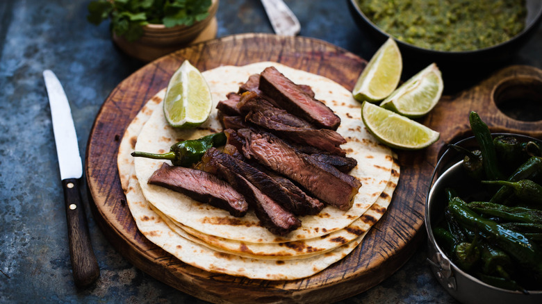 carne asada taco with limes on a wooden plank