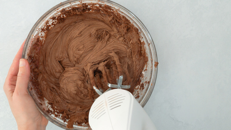 Chocolate buttercream being mixed in a bowl with an electric mixer