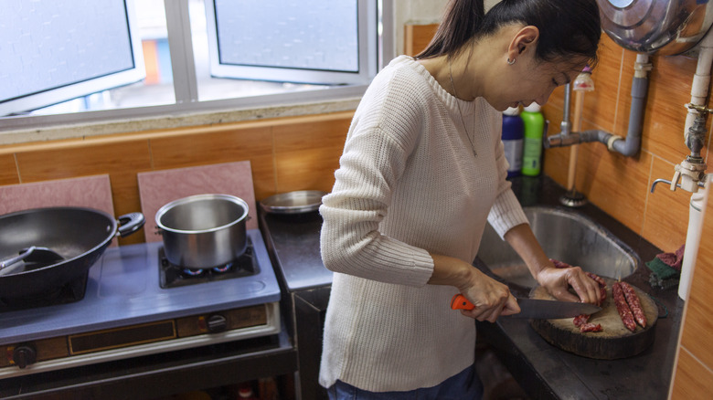Woman cutting lap cheong in kitchen