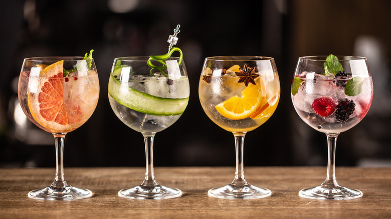 4 cocktails in glasses garnished with oranges, cucumbers, grapefruit, and berries