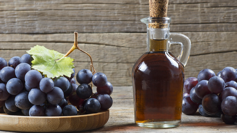 A carafe of vinegar surrounded by wine grapes