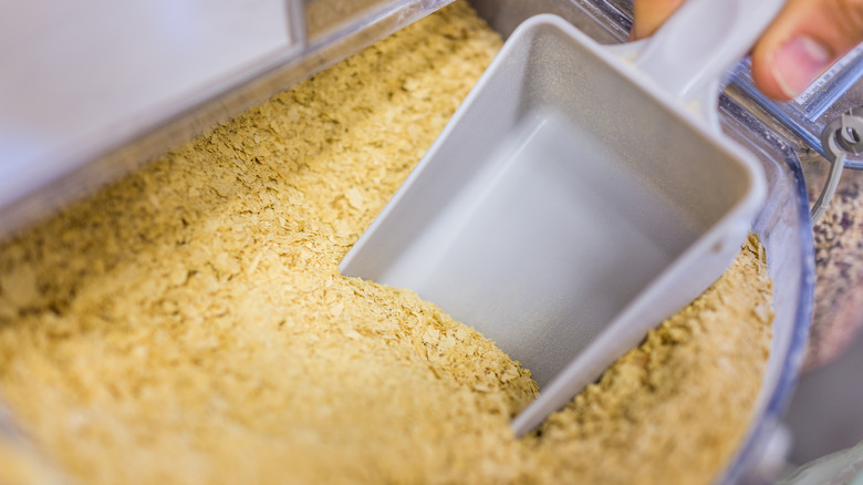 Hand scooping nutritional yeast flakes from a bulk bin