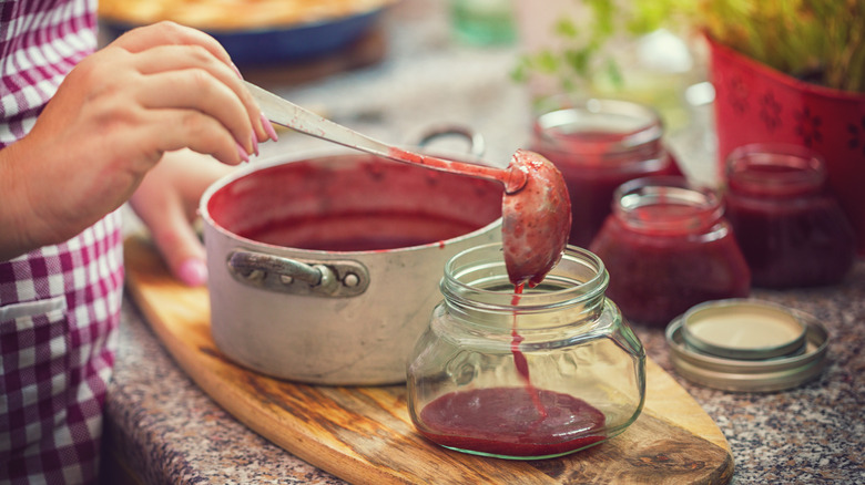 woman spooning homemade jam into a jar